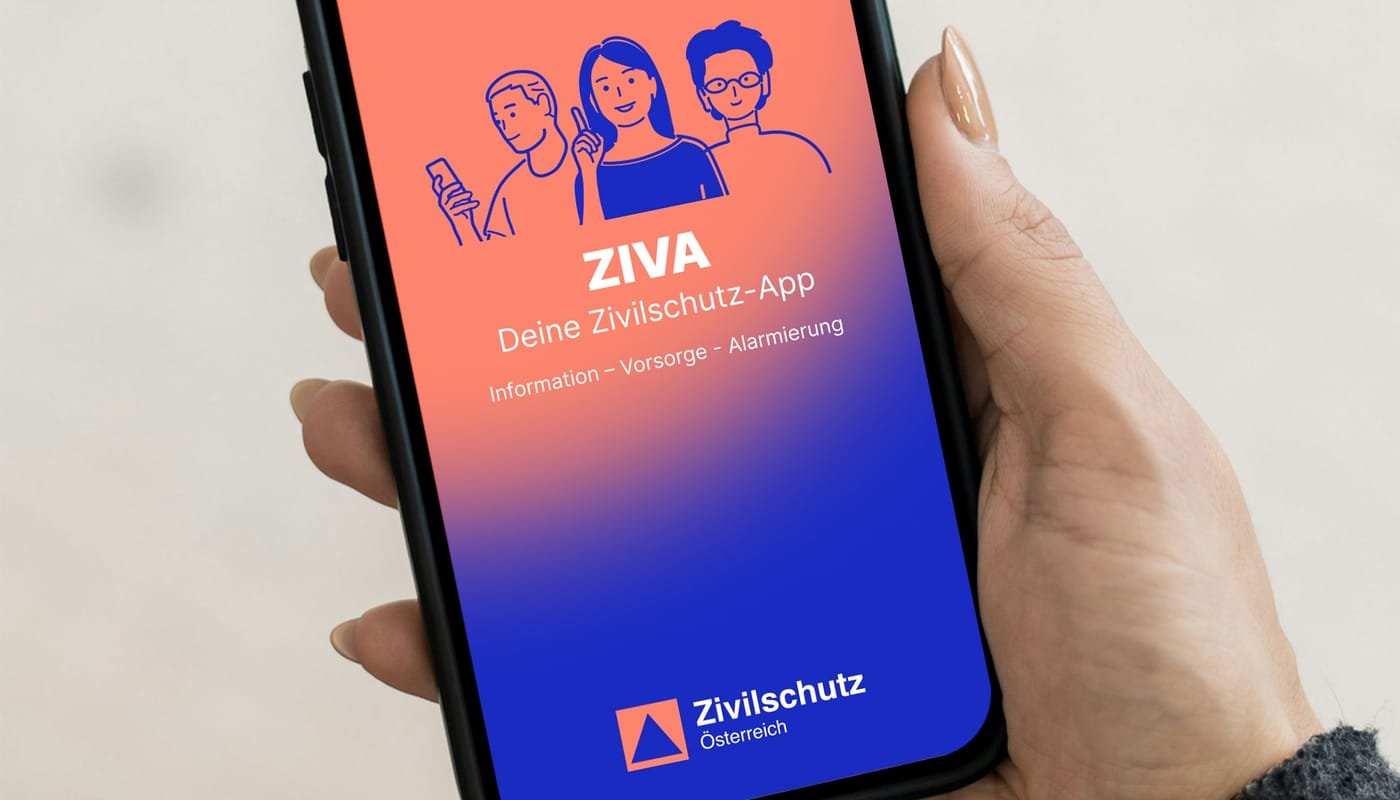 Hand hält ein Smartphone mit dem Startbildschirm der ZIVA-App: Illustration von drei Menschen, Schriftzug „ZIVA – Deine Zivilschutz-App“, darunter „Information – Vorsorge – Alarmierung“